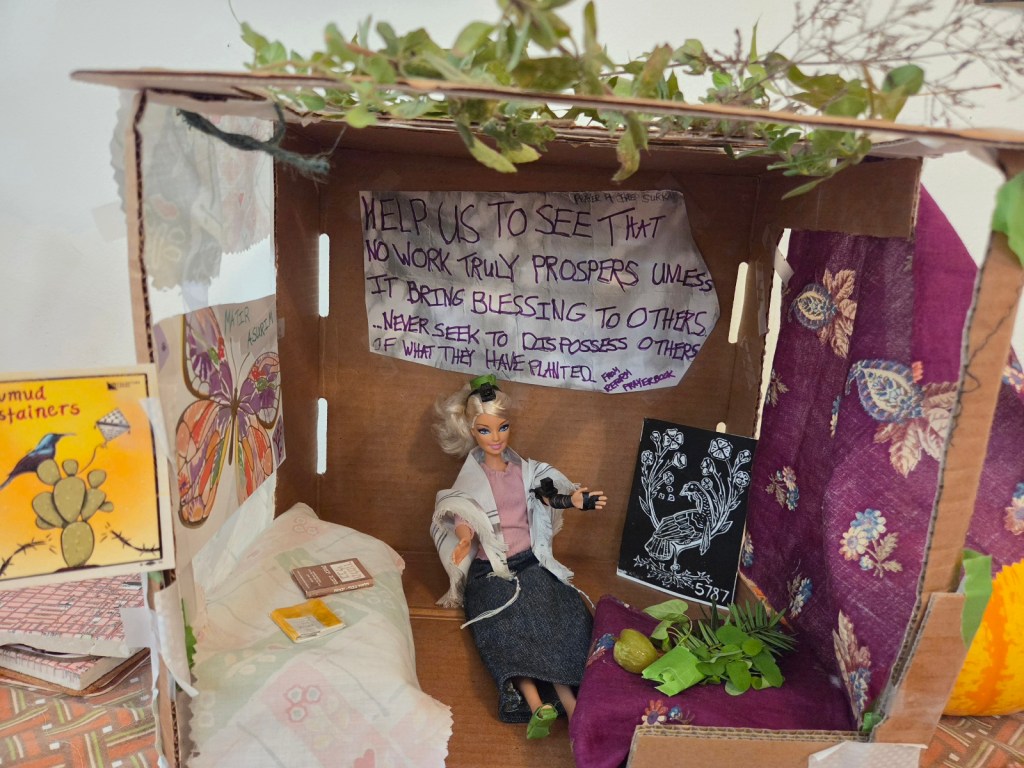 DC Tefillin Barbie in her cardboard and cloth sukkah with dried greenery roofing. Tefillin Barbie wears store-bought clothing, tallit and tefillin crafted by soferet Jen Taylor Friedman plus homemade kippah and shoes. Furnishings and lulav and etrog are homemade. More details in post.