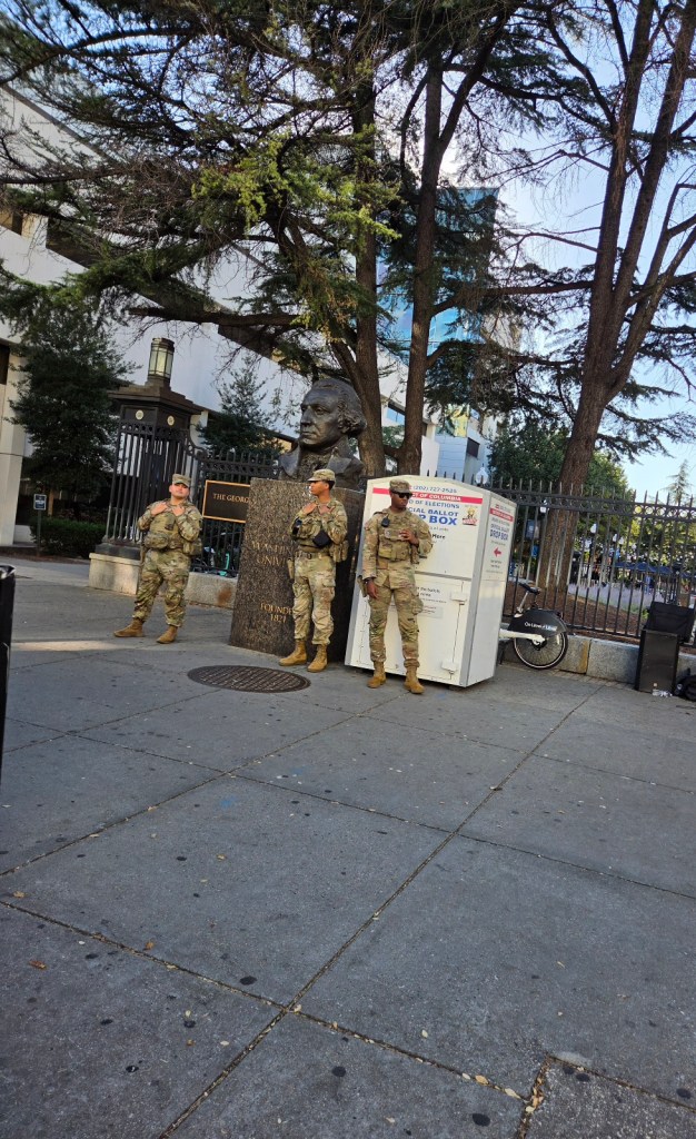 Three National Guard standing at drop box for ballots near Foggy Bottom Metro station and GW University (Northwest DC) at rush hour, October 8, 2026.